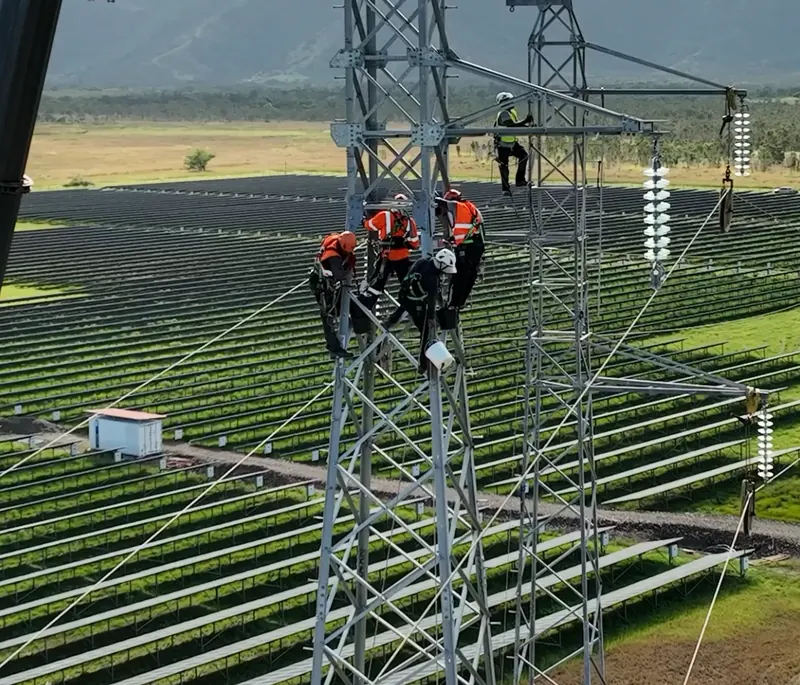 Techniciens sur un pylône électrique au-dessus d’une centrale solaire